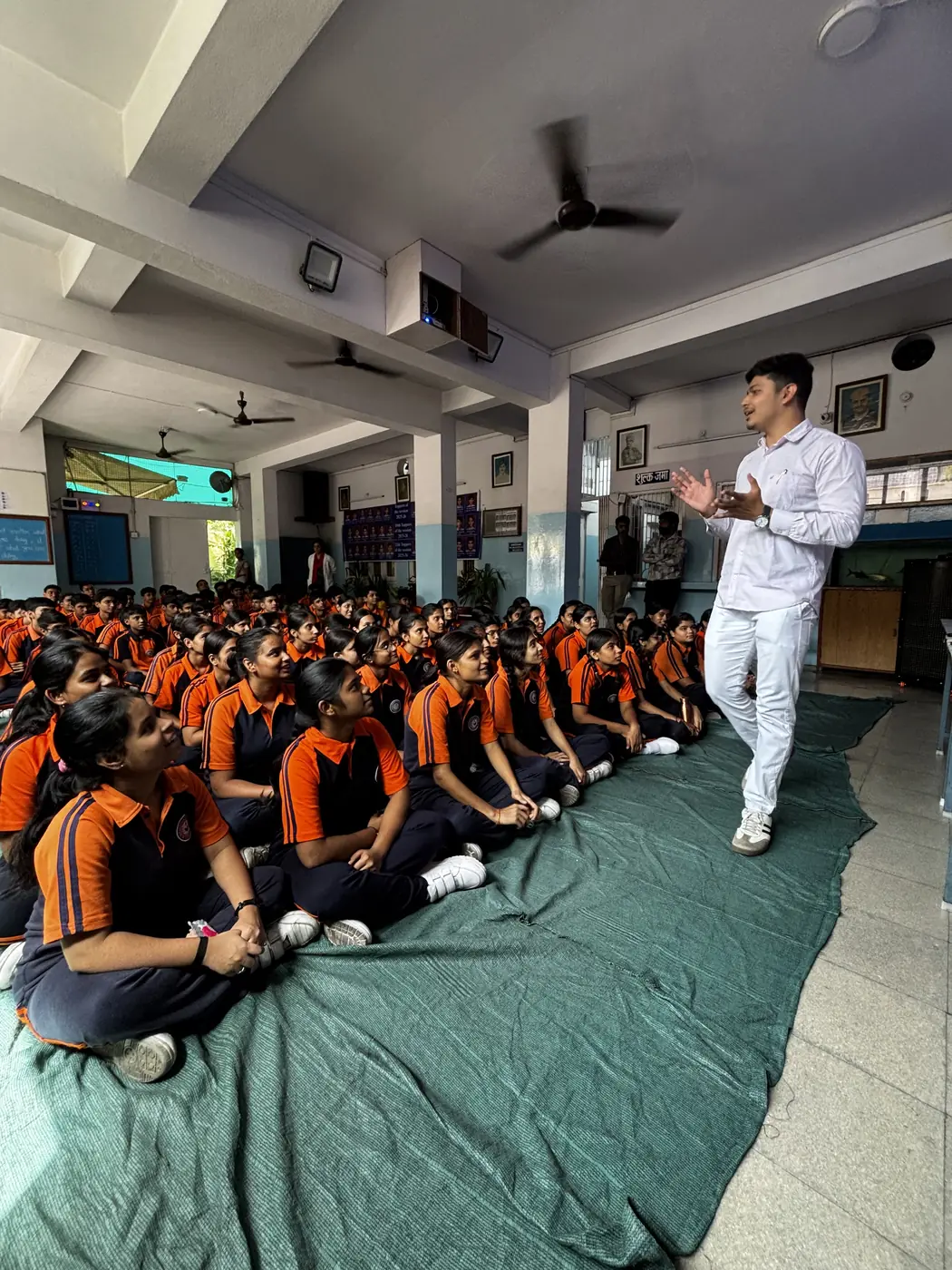 An educator demonstrating to school students seated on the floor of an assembly hall