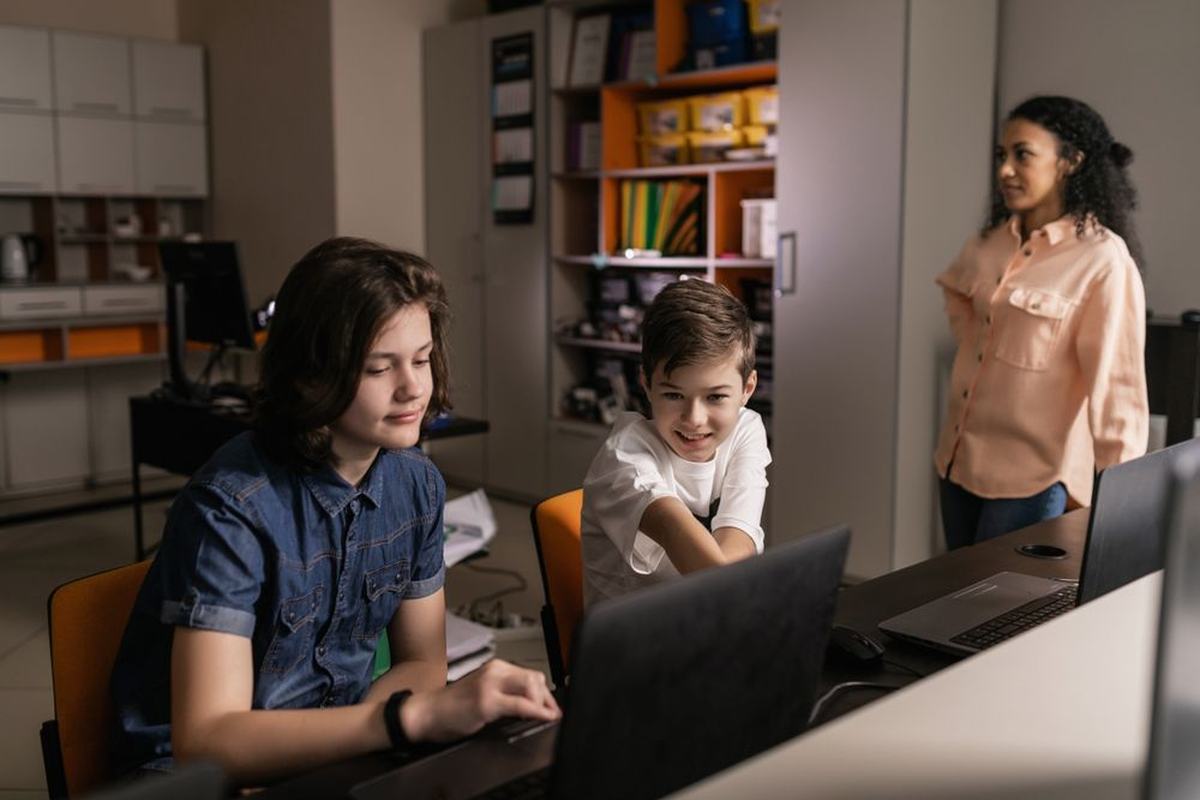 Two students working on a laptop while a teacher looks on in a classroom