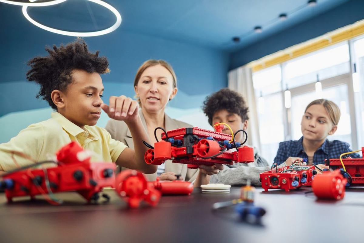 A teacher guiding students who are building red robots in a classroom